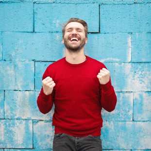 picture of man with read shirt on with a big smile with a background of a blue brick wall